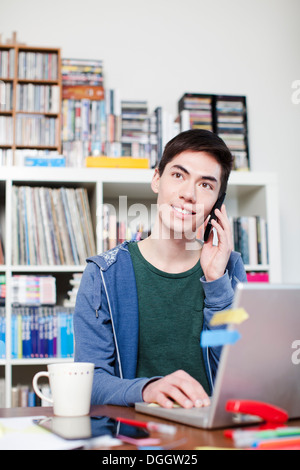 Male student on cell phone using laptop Stock Photo