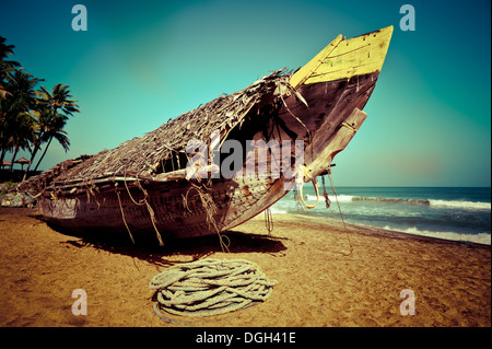 Tropical beach landscape with fishing boat at ocean coast under blue sky. Image in vintage style. India Stock Photo