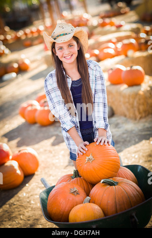 Preteen Girl Wearing Cowboy Hat Playing with a Wheelbarrow at the Pumpkin Patch in a Rustic Country Setting. Stock Photo