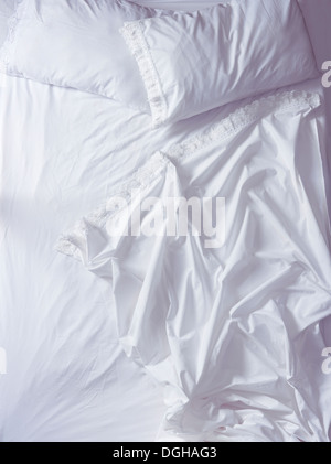 Empty unmade bed with ruffled white sheets in morning light, high angle view. Stock Photo