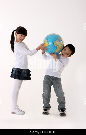 East Asian boy and girl carrying a globe on the shoulders, smiling, looking at the camera Stock Photo