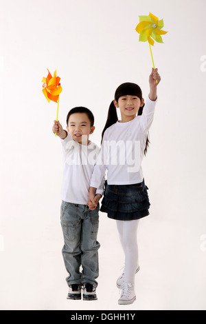 East Asian boy and girl playing with paper windmills, hand in hand, smiling, looking at the camera Stock Photo