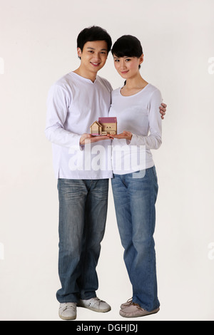 East Asian couple embracing, holding a model house, standing on the floor Stock Photo