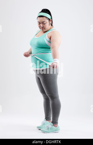 a fat girl in a gym outfit measuring herself dghrtk