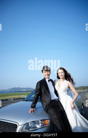 newlyweds leaning on a car Stock Photo