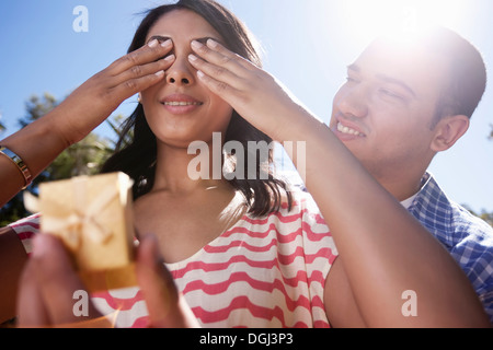 Young woman covering eyes with hands, man holding ring box Stock Photo