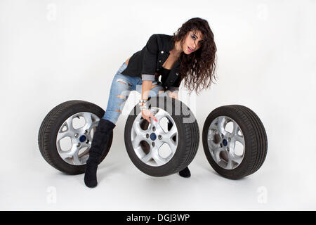 Young woman wearing a short jacket, jeans and boots, posing with car wheels Stock Photo