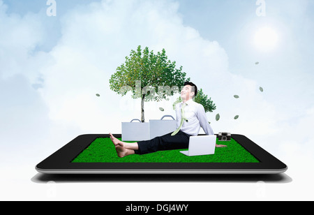 a man sitting on a tablet under a tree Stock Photo