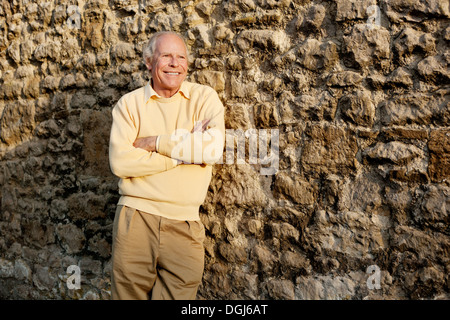 Senior man leaning against stone wall with arms crossed Stock Photo