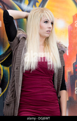 Young woman with long blonde hair posing in front of a wall with graffiti Stock Photo