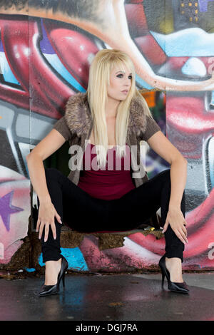 Young woman with long blonde hair posing in front of a wall with graffiti Stock Photo