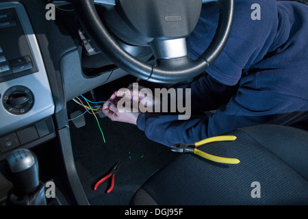 A man wearing a hoody hot wiring a car. Stock Photo