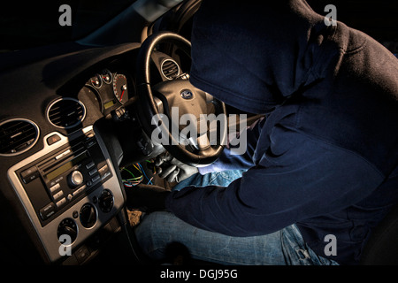 A man wearing a hoody hot wiring a car. Stock Photo