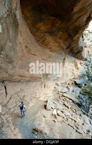 Local hiker walking under a rock overhang on the path to the abandoned settlement of Sap Bani Khamis on the western flank of the Stock Photo