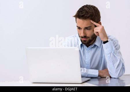 Young man sitting at desk looking at laptop Stock Photo