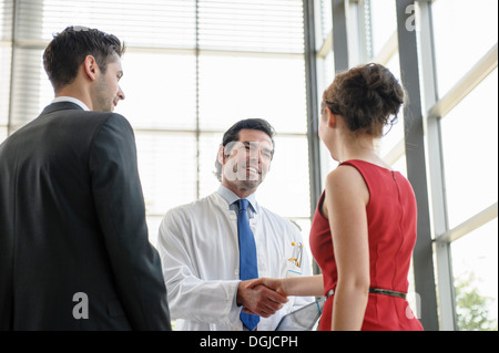 Mature doctor shaking hands with young couple in hospital lobby Stock Photo
