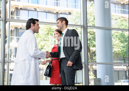 Mature doctor shaking hands with young couple in hospital lobby Stock Photo