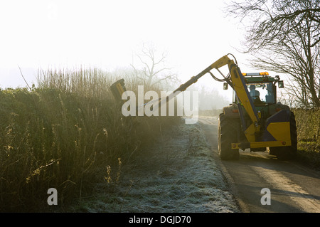 Tractor cutting hedge along country road Stock Photo