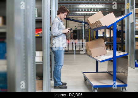 Female warehouse worker checking orders on distribution trolley Stock Photo