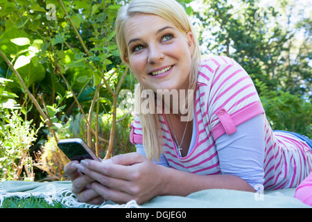 Woman lying on blanket in garden using cell phone Stock Photo