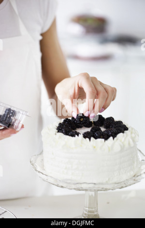 Woman decorating cake with fresh blackberries Stock Photo