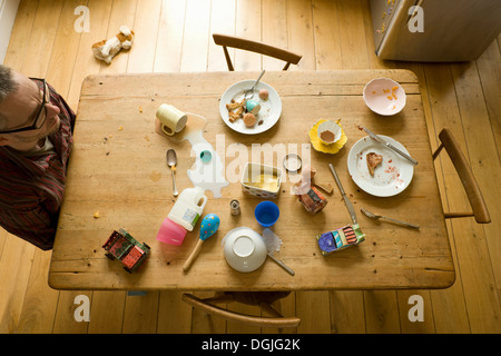 Overhead view of mature man sitting alone at messy breakfast table