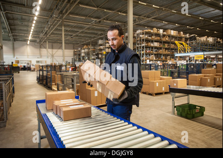 Male warehouse worker selecting cardboard boxes from conveyor belt Stock Photo