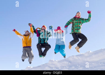 Four young people wearing colourful winter clothes jumping over a snow-covered ridge, Flachau, Salzburg, Austria, Europe Stock Photo