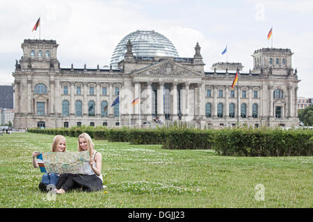 Two young women studying a map of Berlin, sitting on a lawn in front of the Reichstag building, Berlin Reichstag, Berlin, Berlin Stock Photo