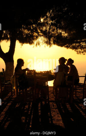 Three women sitting at a table in a seaside garden at sunset, Lefkas, Greece, Europe Stock Photo