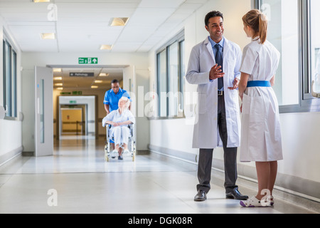 Asian Indian male doctor & female nurse in hospital corridor & senior female wheelchair patient & African American nurse Stock Photo