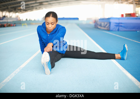 Young female athlete sitting on floor touching toes Stock Photo