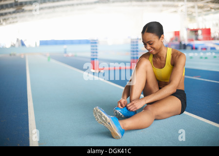 Young female athlete sitting on floor tying shoelace Stock Photo