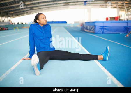 Young female athlete sitting on floor stretching legs Stock Photo