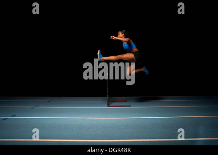 Young female athlete jumping hurdle Stock Photo