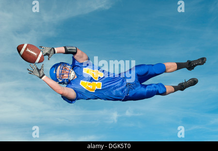 American footballer catching ball against blue sky Stock Photo