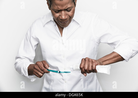 Senior woman struggling to squeeze toothpaste onto toothbrush Stock Photo