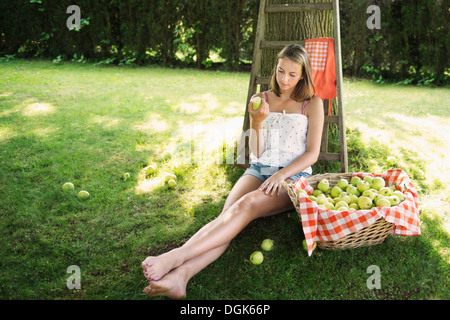 Adolescent girl sitting in orchard eating an apple Stock Photo