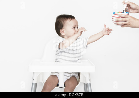 Baby boy sitting in highchair reaching for food Stock Photo