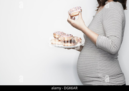 Pregnant woman holding plate of doughnuts Stock Photo