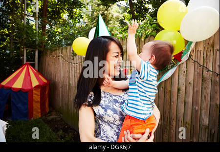 Mother wearing party hat holding baby boy at birthday party Stock Photo
