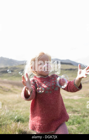 Young girl with eyes closed running to catch bubbles Stock Photo
