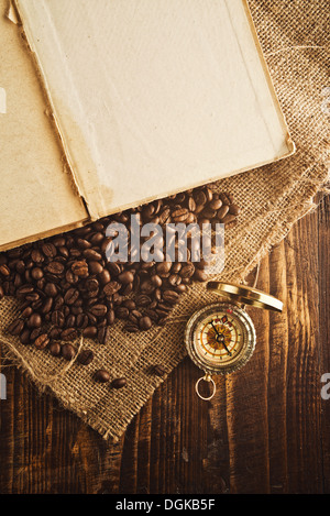 Coffee beans and compass on open book on jute canvas texture. Stock Photo