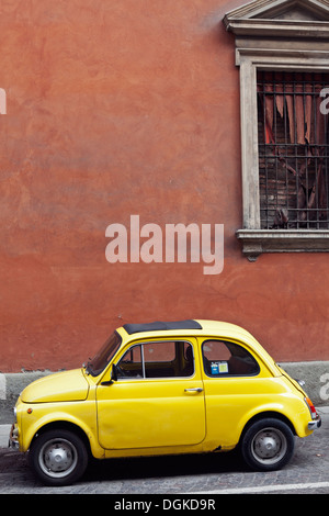 A vintage yellow Fiat 500 car parked on a cobbled street in front of an ochre wall in Bologna. Stock Photo