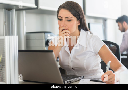 Woman working in office, man in background Stock Photo