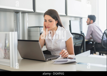 Woman working in office, man in background Stock Photo