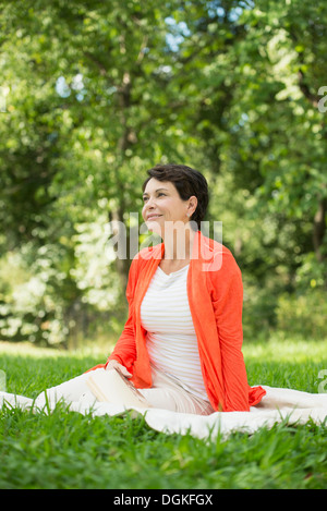 Mature woman sitting on grass in park Stock Photo