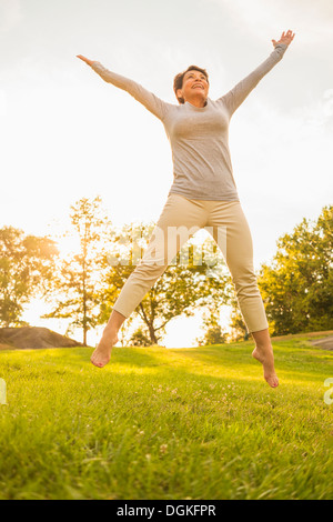 Mature woman jumping on grass Stock Photo