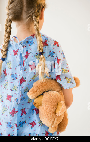 Rear view of blond girl (8-9) in hospital holding teddy bear Stock Photo