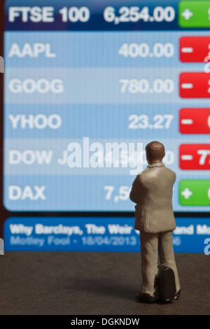 Toy business figure looking at FTSE 100 Index screen. Stock Photo